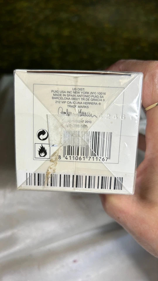 Close-up of a product box with text and a barcode, held by a hand against a blurred background.