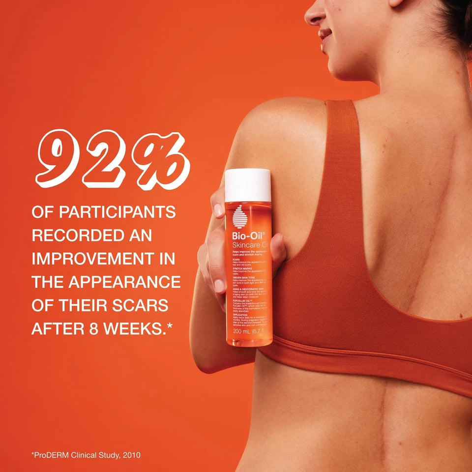 Woman holding a bottle of Bio-Oil Skincare on an orange background with text about scar improvement.